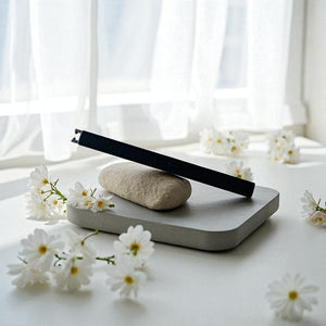 Concrete tray with a black rechargeable lighter and white flowers on a white surface with white curtains in the background