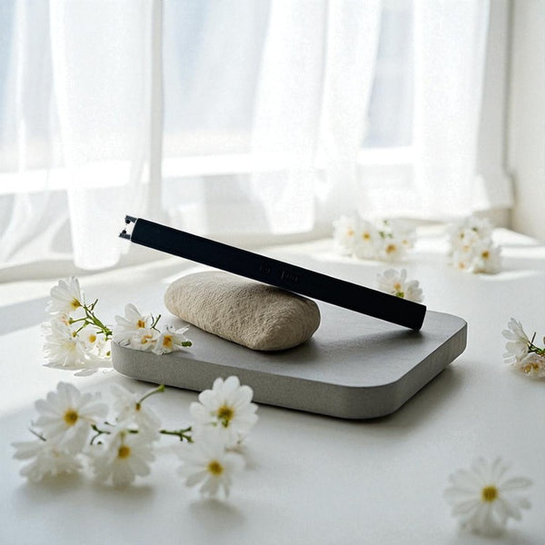Concrete tray with a black rechargeable lighter and white flowers on a white surface with white curtains in the background