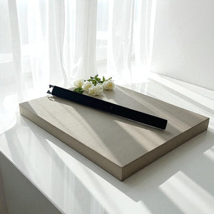 Wooden tray with a black rechargeable lighter and white flowers on a white surface with white curtains in the background