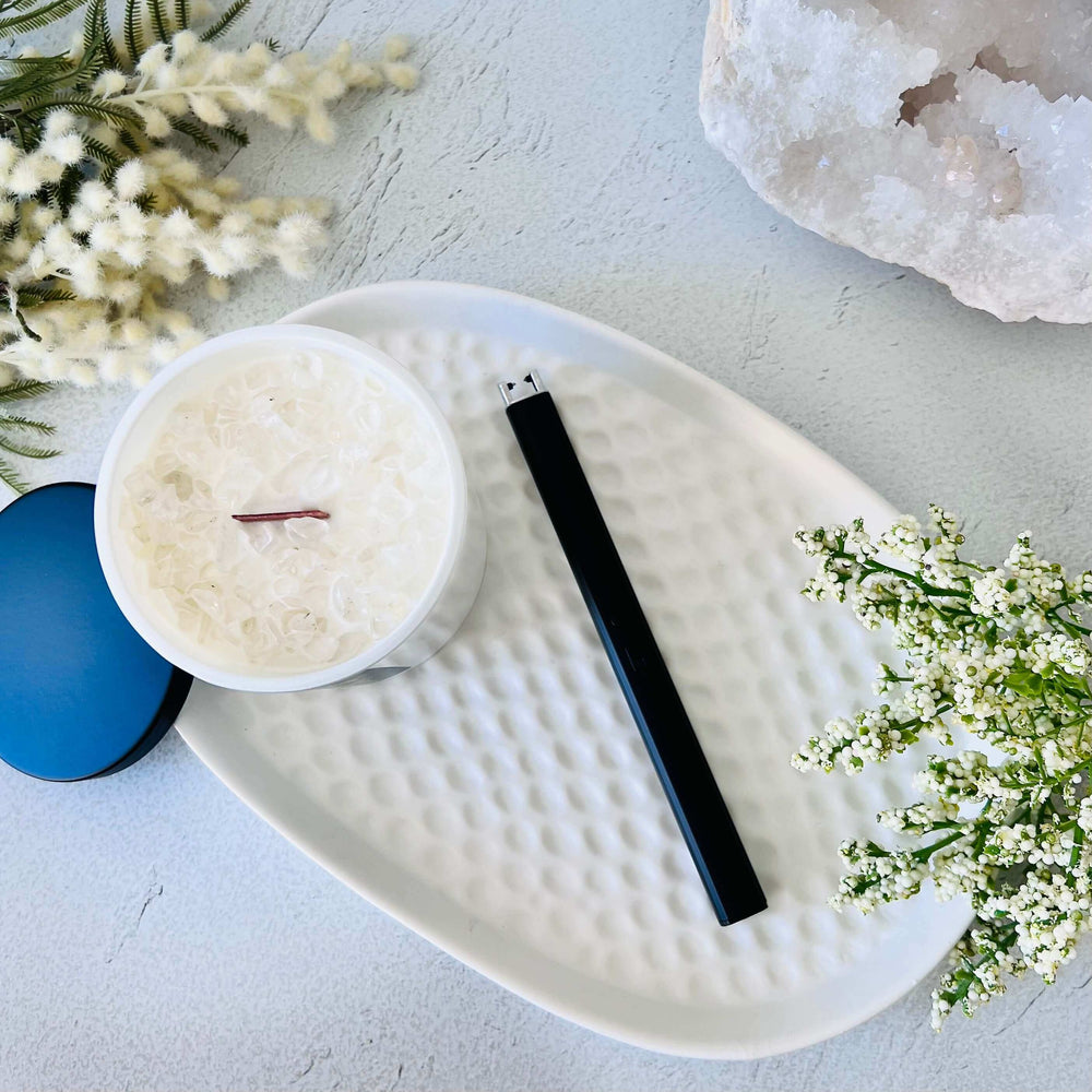 Concrete tray with a black rechargeable lighter and white flowers on a white surface with white curtains in the background