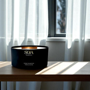 Black SOJA candle on a wooden surface with curtains in the background