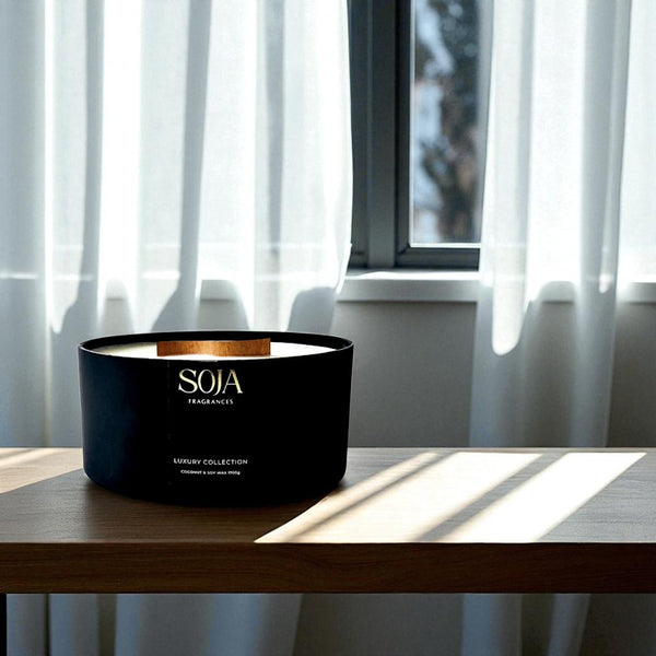 Black SOJA candle on a wooden surface with curtains in the background