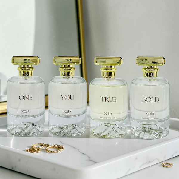 Four SOJA perfume bottles labeled 'ONE', 'YOU', 'TRUE', and 'BOLD' on a marble surface.