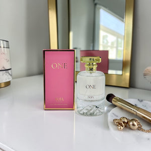 Perfume bottle labeled 'ONE' with pink packaging and makeup items on a marble surface.
