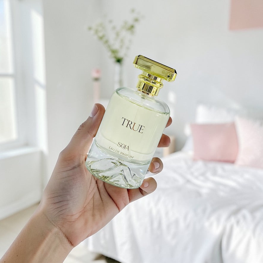 Hand holding a 'True' perfume bottle with a blurred indoor background