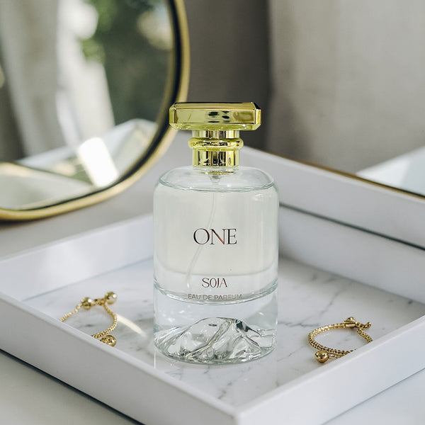 Perfume bottle labeled 'ONE SOIA' on a marble surface with jewelry.