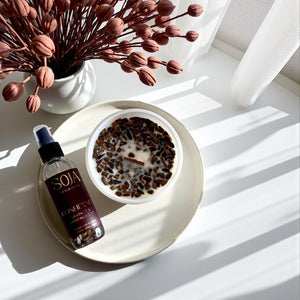 Candle and room spray leather and sandalwood product showing tigers eye crystals on a white surface with a tray  and dried flowers.