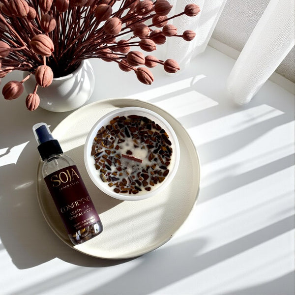 Candle and room spray leather and sandalwood product showing tigers eye crystals on a white surface with a tray  and dried flowers.