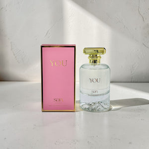 Perfume bottle and packaging with 'YOU' branding on a light surface.