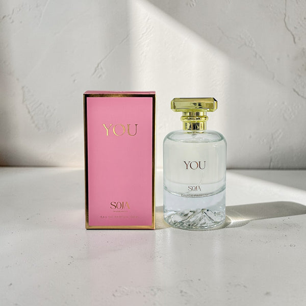 Perfume bottle and packaging with 'YOU' branding on a light surface.