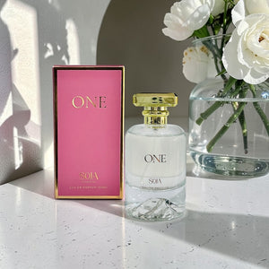 Perfume bottle and packaging with a vase of white flowers on a light surface