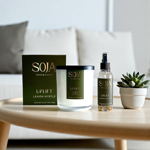SOJA Fragrances candle, room spray, and box on a table with a plant in the background
