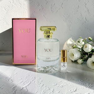 Perfume bottle with pink packaging and flowers on a textured surface