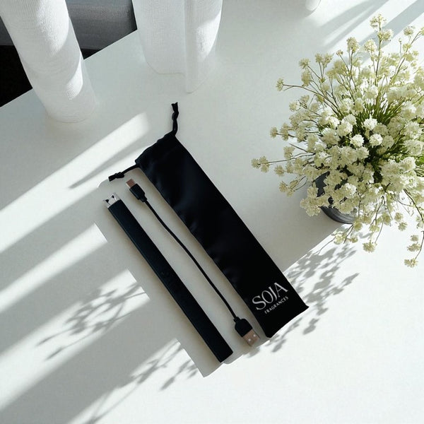 Black pouch with 'SOJA' branding on a white surface with a vase of white flowers.