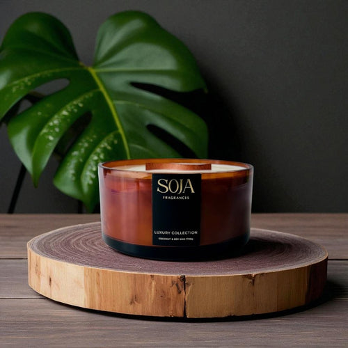 Candle in a glass holder with wooden base on a dark surface, featuring the brand 'SOJA'.