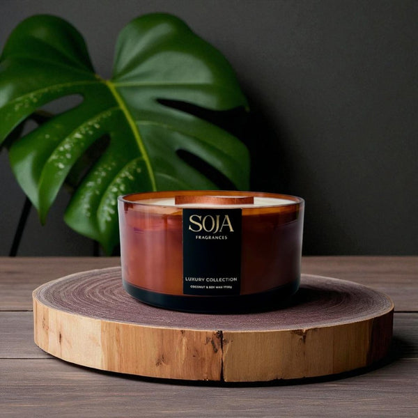 Candle in a glass holder with wooden base on a dark surface, featuring the brand 'SOJA'.