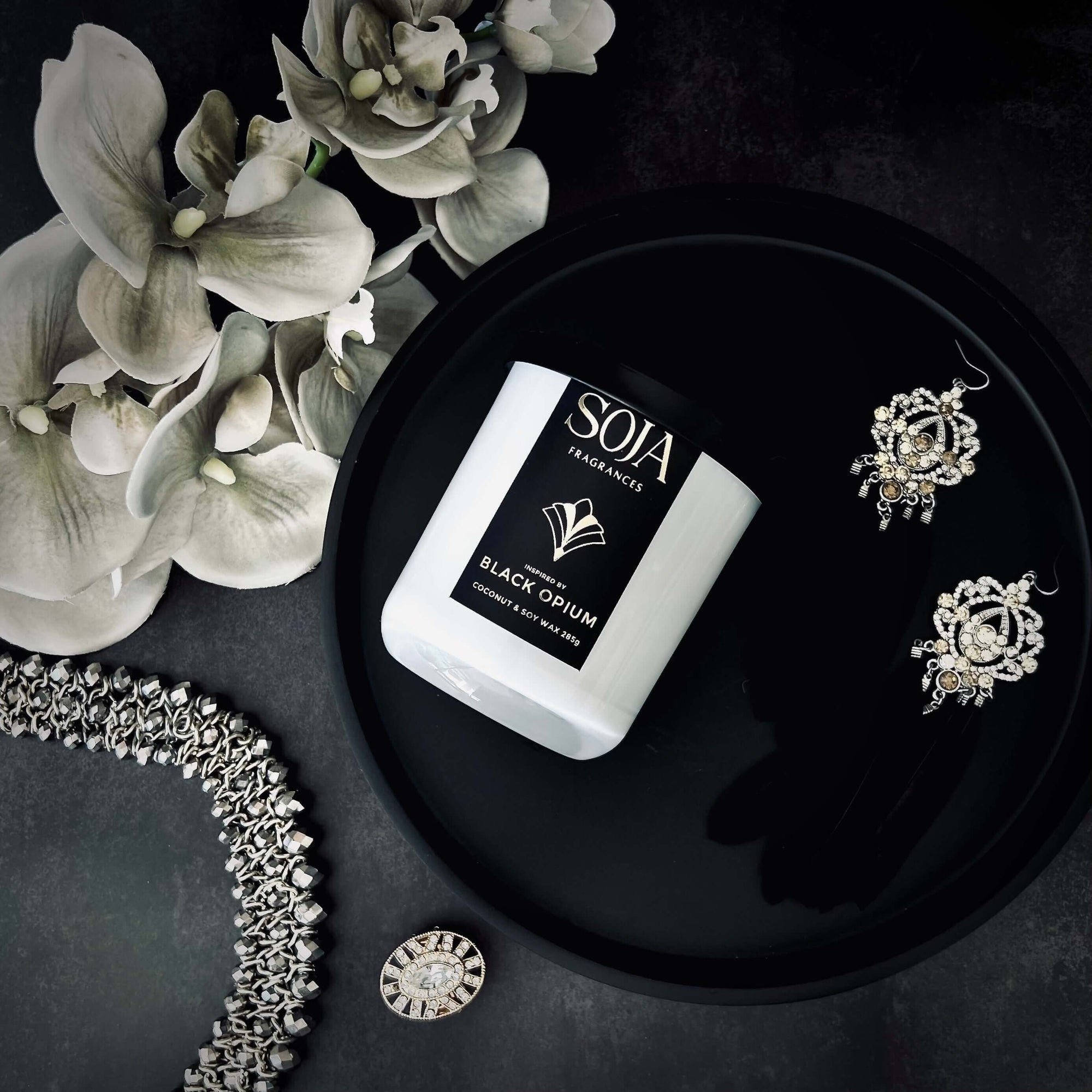 Black opium perfumed candle 285 grams on black tray with white orchids and diamond jewellery