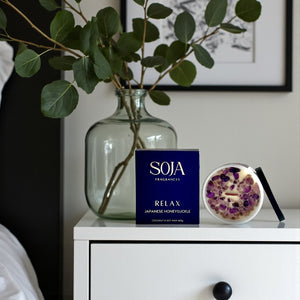 SOJA Fragrances Relax candle on a white surface with a vase and plant in the background