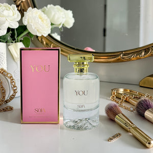 Perfume bottle and packaging labeled 'YOU' on a table with decorative items.
