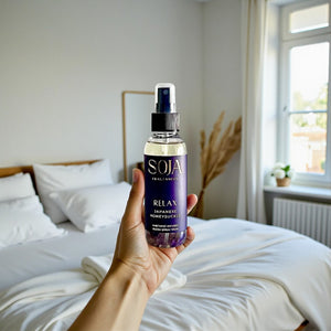 Hand holding a bottle of SOJA Fragrances room spray in a bedroom setting