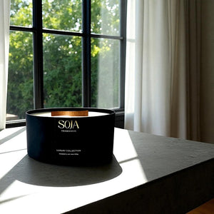Black SOJA Fragrances candle on a windowsill with greenery outside